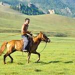 Mongolian nomad wrangler with urga pole on horseback in Terelj